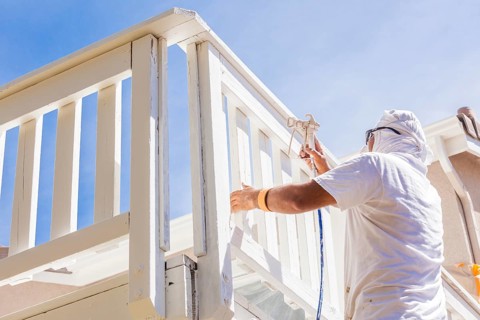 House painter wearing facial protection spray painting A deck of A home