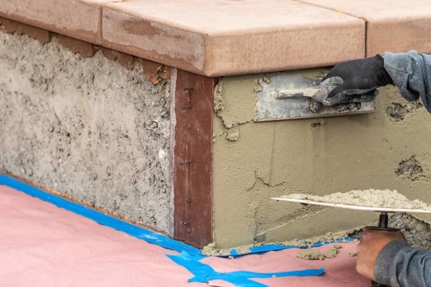 Tile worker applying cement with trowel at pool construction site