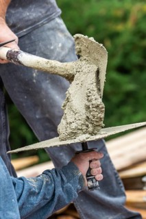 Construction worker placing wet cement on platter for tile worker at pool construction site