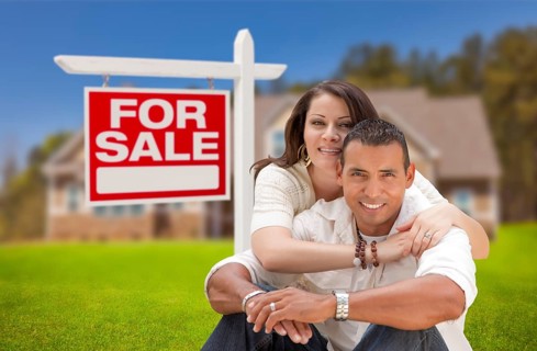 Young happy hispanic young couple in front of their new home and for sale real estate sign