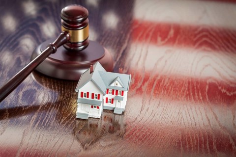 Small house and gavel on wooden table with american flag reflection