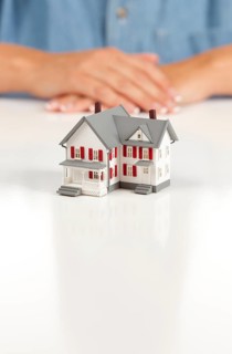 Womans folded hands behind model house on white surface