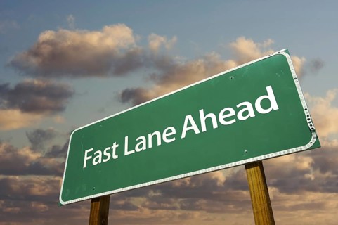 Fast lane ahead green road sign over dramatic clouds and sky