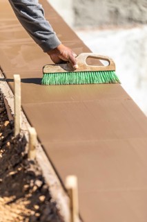 Construction worker using brush on wet cement forming coping around new pool