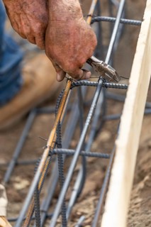 Worker securing steel rebar framing with wire plier cutter tool at construction site