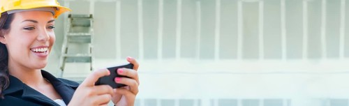 Female contractor wearing hard hat using cell phone against dywall banner background with ladder
