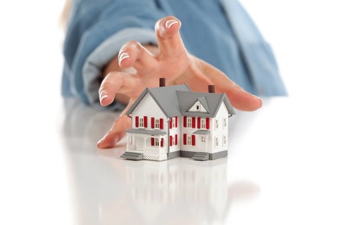 Womans hand reaching for model house on a white surface
