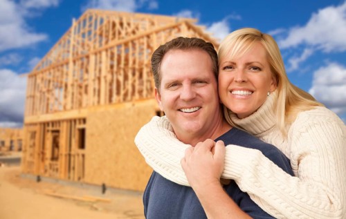 Happy excited couple in front of their new home construction framing site
