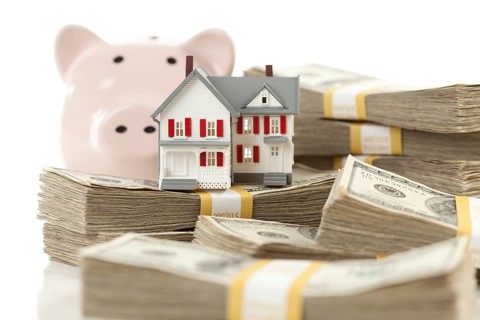 Small house and piggy bank with stacks of hundred dollar bills isolated on a white background