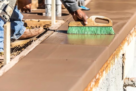 Construction worker using brush on wet cement forming coping around new pool