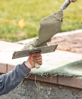Construction worker placing wet cement on platter for tile worker at pool construction site