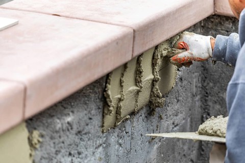 Tile worker applying cement with trowel at pool construction site