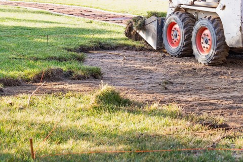 Small bulldozer removing grass from yard preparing for pool installation