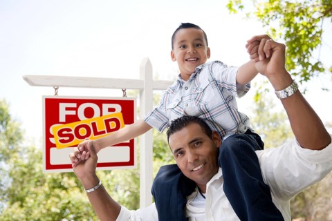 Excited hispanic father and son in front of sold for sale real estate sign