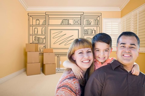 Happy young mixed-race family in room with moving boxes and drawing of entertainment unit on wall