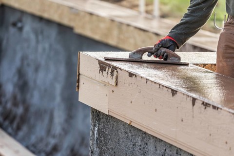Construction worker using wood trowel on wet cement forming coping around new pool