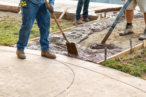 Construction worker pouring wet deck cement into wooden frame