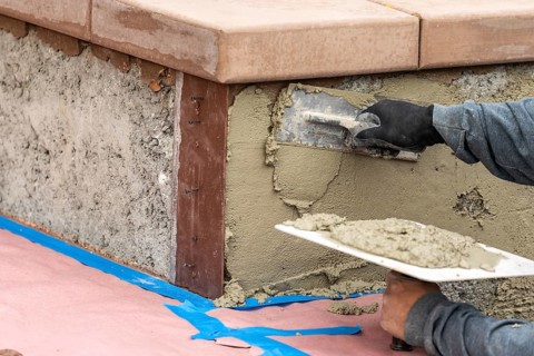 Tile worker applying cement with trowel at pool construction site