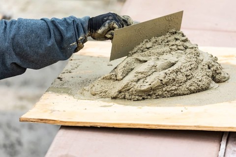 Tile worker mixing wet cement on board at pool construction site