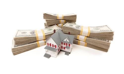 Small house with stacks of hundred dollar bills isolated on a white background