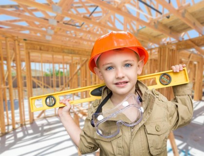 Young boy contractor with level on site inside new home construction framing
