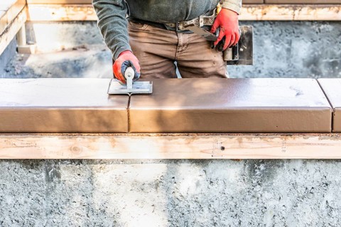 Construction worker using hand groover on wet cement forming coping around new pool