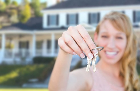 Excited female holding house keys in front of nice new home