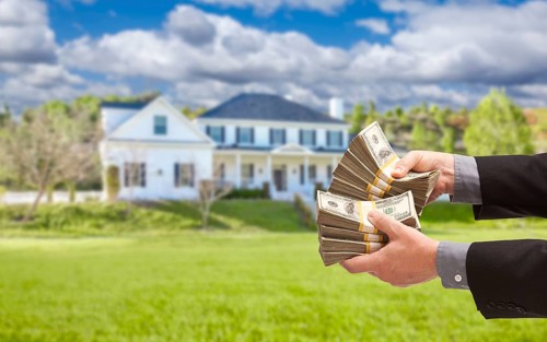 Man handing over thousands of dollars in front of beautiful house