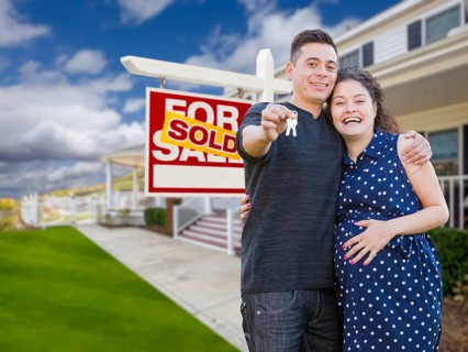 Happy hispanic couple in front of new home and sold real estate sign showing off their house keys