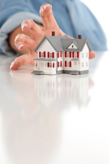 Womans hand reaching for model house on a white surface