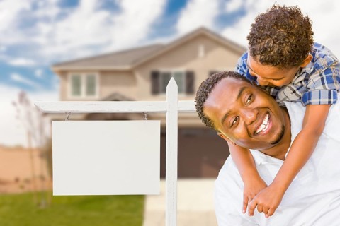 Happy african american father and mixed-race son in front of blank real estate sign and new house