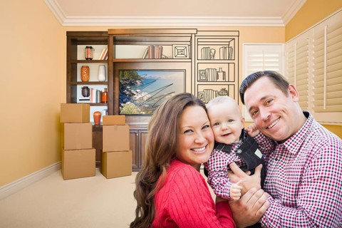 Young family in room with moving boxes and drawing of entertainment unit on wall