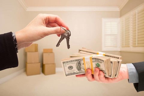 Man and woman handing over cash for house keys inside empty tan room with boxes