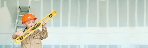 Cute young boy dressed as contractor holding level against dywall banner background with ladder