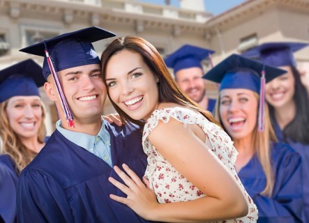 Proud male graduate in cap and gown with girl among other graduates behind