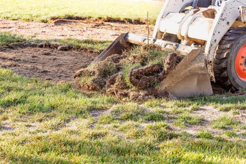 Small bulldozer removing grass from yard preparing for pool installation