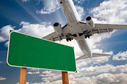 Blank green road sign and airplane above with dramatic blue sky and clouds