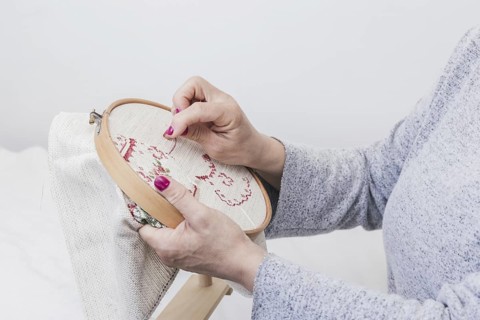 woman s hand cross stitching pattern on a hoop against white background