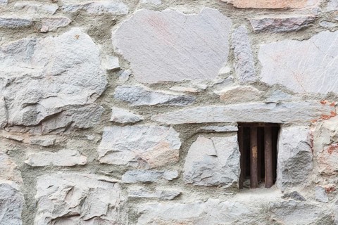 Old stone wall with small iron barred prison cell window