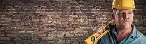 Male contractor in hard hat holding level in front of old brick wall banner with copy space