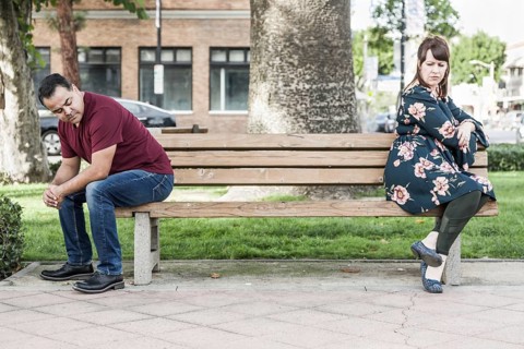 Unhappy mixed-race couple sitting facing away from each other on park bench