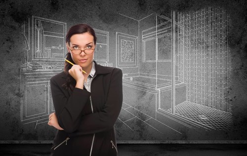 Young adult woman with pencil in front of bathroom design drawing on wall