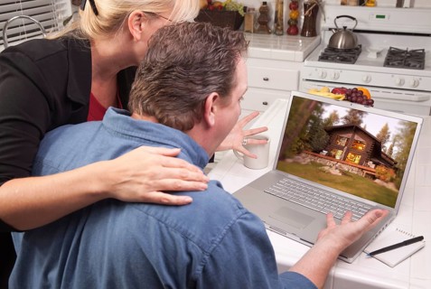 Couple in kitchen using laptop with lake cabin on the screen
