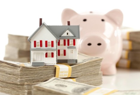 Small house and piggy bank with stacks of hundred dollar bills isolated on a white background