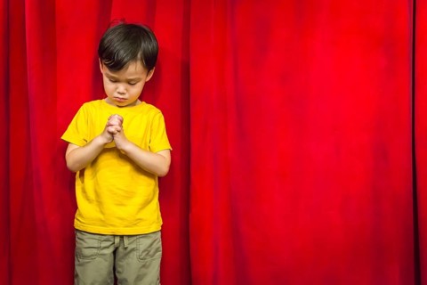 mixed-race boy with praying hands in front of red curtain