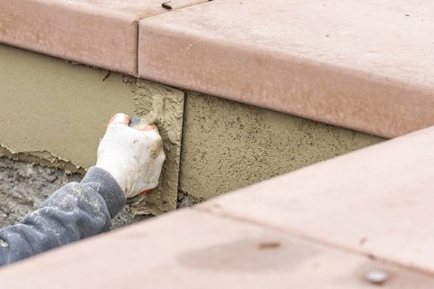 Tile worker applying cement with trowel at pool construction site