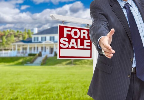 Real estate agent reaches for handshake with sale sign and new house behind