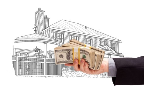 Hand holding thousands of dollars in cash over house drawing