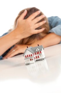 Woman with head in hand behind model home on a white surface