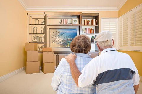 Senior couple in room with moving boxes looking at drawing of entertainment unit